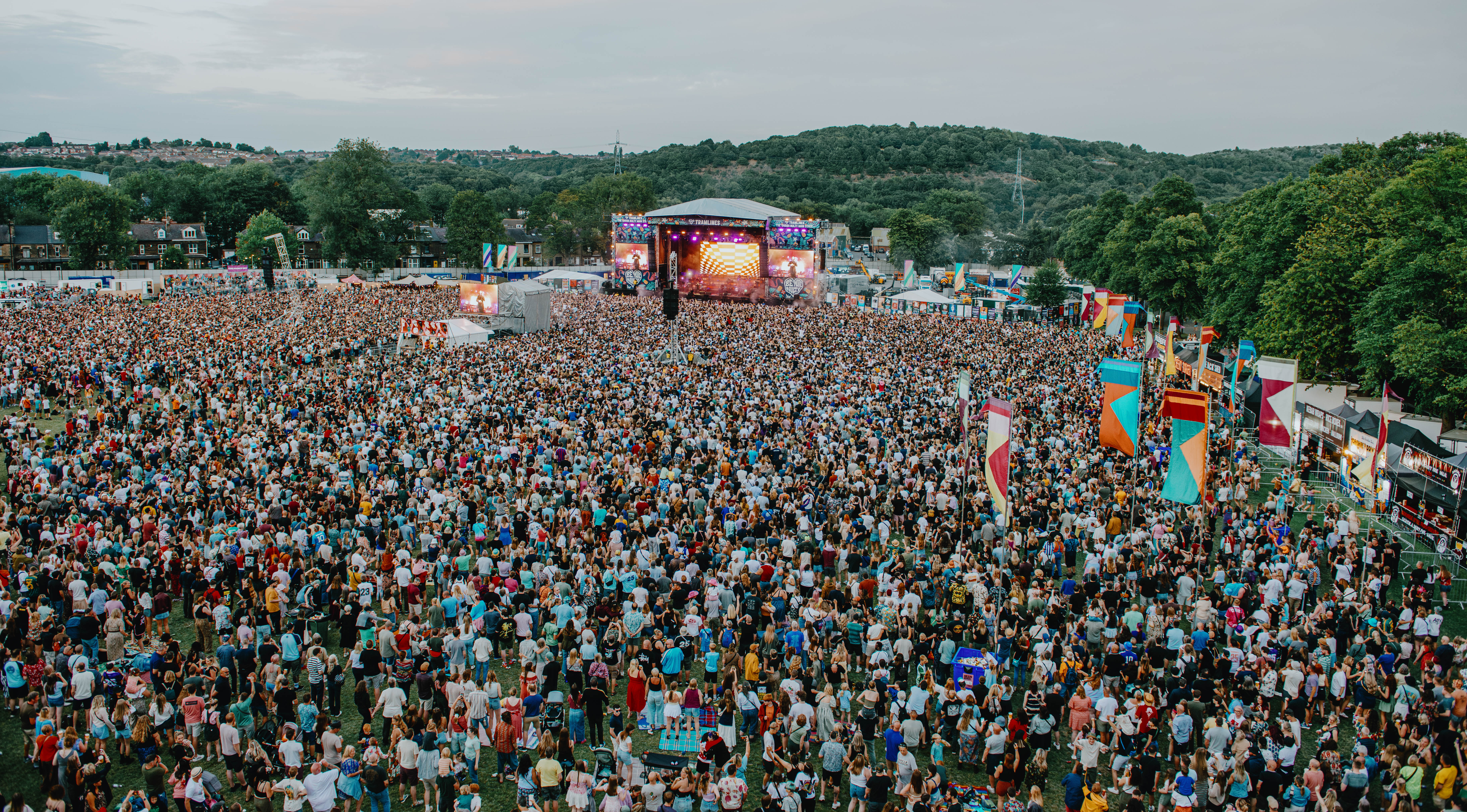 Aerial shot looking down on Hillsborough Park with a crowd of thousands of people in front of main stage of Tramlines as stage lights  beam out