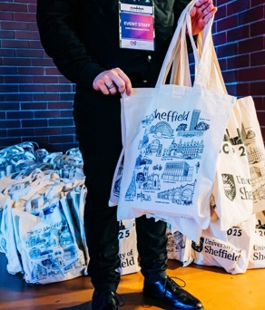 People standing around a long table covered with rows of name badges, selecting or searching for their badges in a modern event registration area.