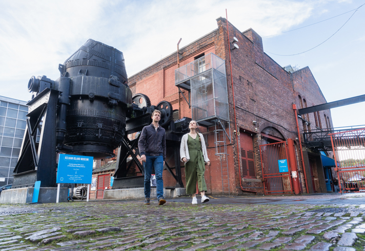 A couple walking in front of the bessemer converter at kelham island museum 