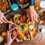 Overhead view of people sharing a variety of bar food, sliders, nachos, and drinks.