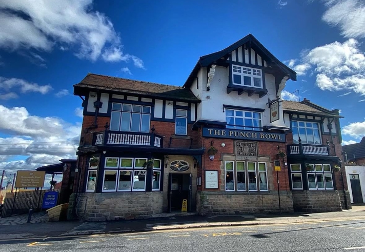 The exterior of The Punch Bowl pub in Crookes, a large traditional brick building with white and black timber detailing, set against a bright blue sky.