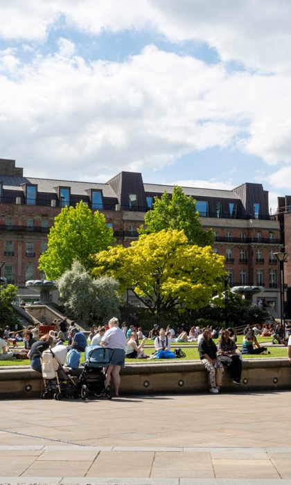 Lots of people enjoying a warm sunny day in The Peace Gardens. In the background is The Radison Blu Hotel.