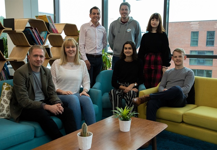 A group of seven men and women pose for a photo in an office.