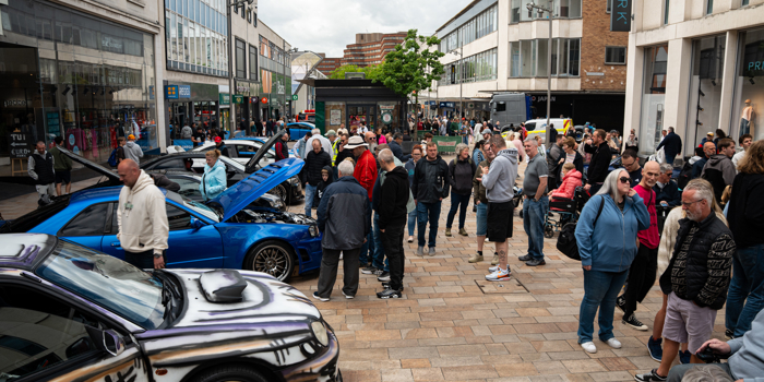 The custom car show from a previous year, with crowds of people looking around cars on display.