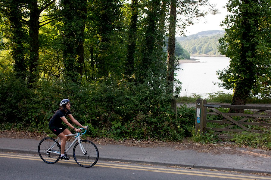 A cyclist riding on the road alongside Damflask Reservoir.