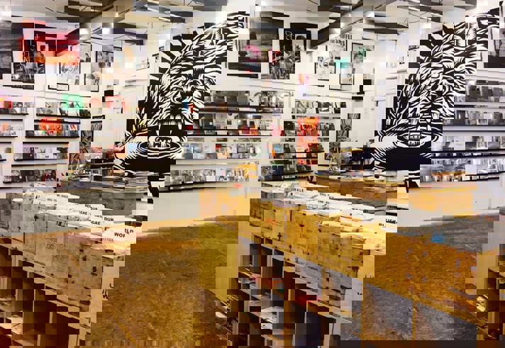 Inside Bear Tree Record, there are rows of wooden units holding records. On the walls new releases are displayed. One section of the wall has a floor to ceiling mural of the Bear Tree Records logo, painted by Sheffield artist Tom J Newell.