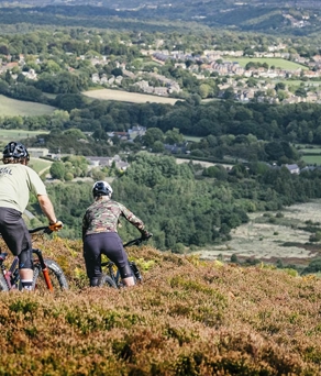 Two people mountain biking through the heather on a hillside above Sheffield.