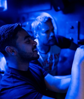 Three people in a room dimly lit by blue light are solving a puzzle at The Great Escape.