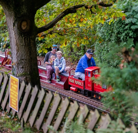 A family rides on a miniature steam train through a wooded area at the Abbeydale Miniature Railway in Sheffield.