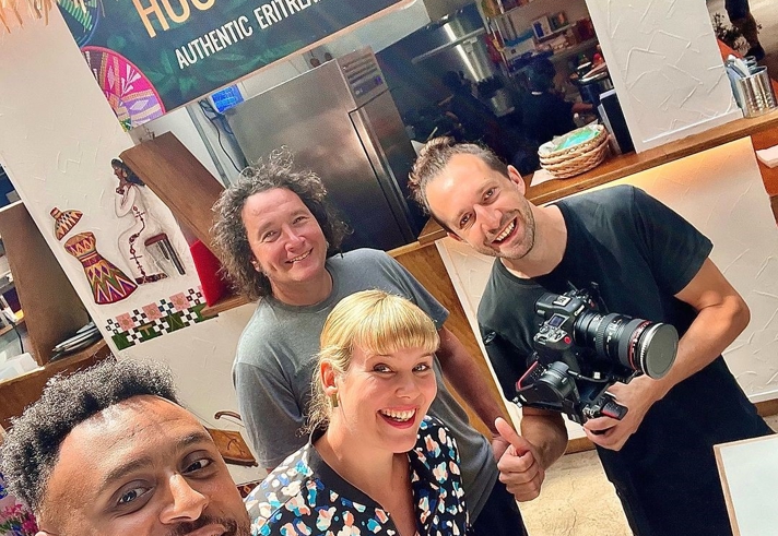 Group of people standing inside a food stall named ‘House of Habesha,’ which has a sign reading ‘Authentic Eritrean & Ethiopian Soul Food.’ The stall features cultural artwork on the walls, and one person is holding a professional camera
