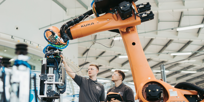 Two people are working on a large robot arm.