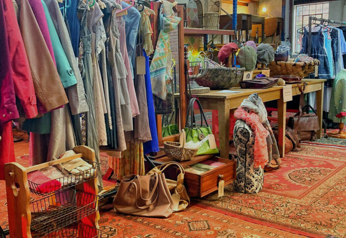 Inside The Warehouse with shelves and tables covered in things to buy and rails full of clothes.