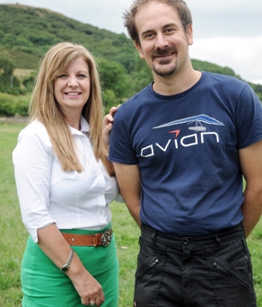 A man and a woman standing in a field. The man is wearing an Avian Hang Gliding branded t-shirt.