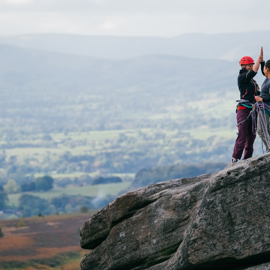 Two people in climbing gear are celebrating on top of a rocky outcrop.