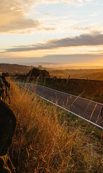 Cyclist riding along countryside road while the sun sets in the background.