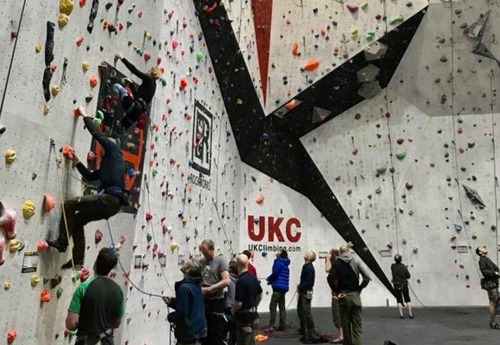 A big climbing wall at Awesome Walls Climbing Centre Sheffield. There are lots people climbing or waiting to climb.