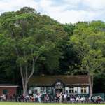 The exterior of Endcliffe Park Cafe. In front of the cafe are tables and chairs where people are enjoying drinks of tea and coffee and meals.