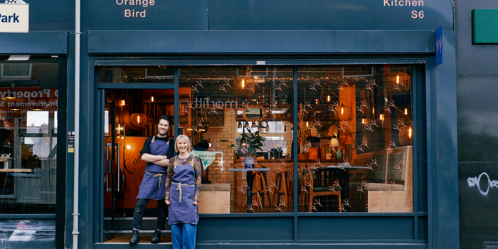 Front view of The Orange Bird restaurant at during the day with two friendly owners standing out front ready to welcome you 