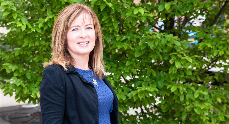 A woman poses for a photo next to a large bush.