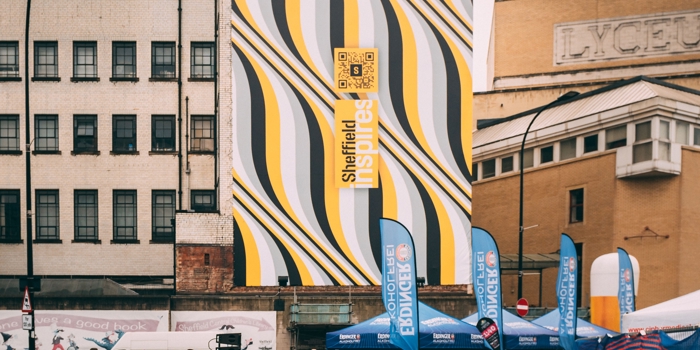 A massive banner on the side of the building shows the distinctive Sheffield Inspires branding as runners gather for Sheffield Half Marathon below it 