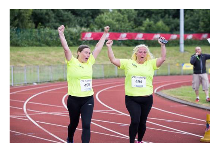 People on a race track, wearing running clothing, with their arms in the air.