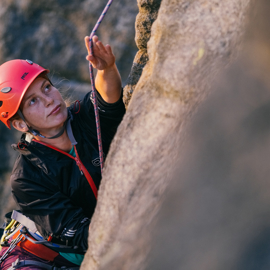 A woman climbing a gritstone rock face.