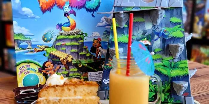 A table at The Dice Box Sheffield with a cocktail, a slice of cake and a game called Dodo.