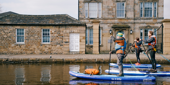 Dan Crawford Outdoors leading a Stand Up Paddleboarding session along Victoria Quays - two participants are following behind as they pass the Sheaf Quay building.