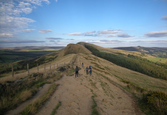 A rough track winding through hills in the countryside. In the distance you can see various groups of people out walking.