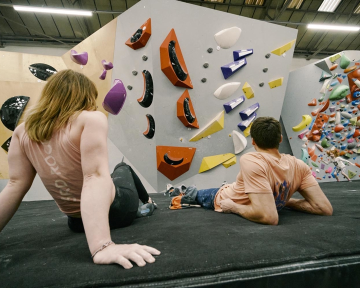 Two people are lying on the floor having a rest at an indoor climbing centre.