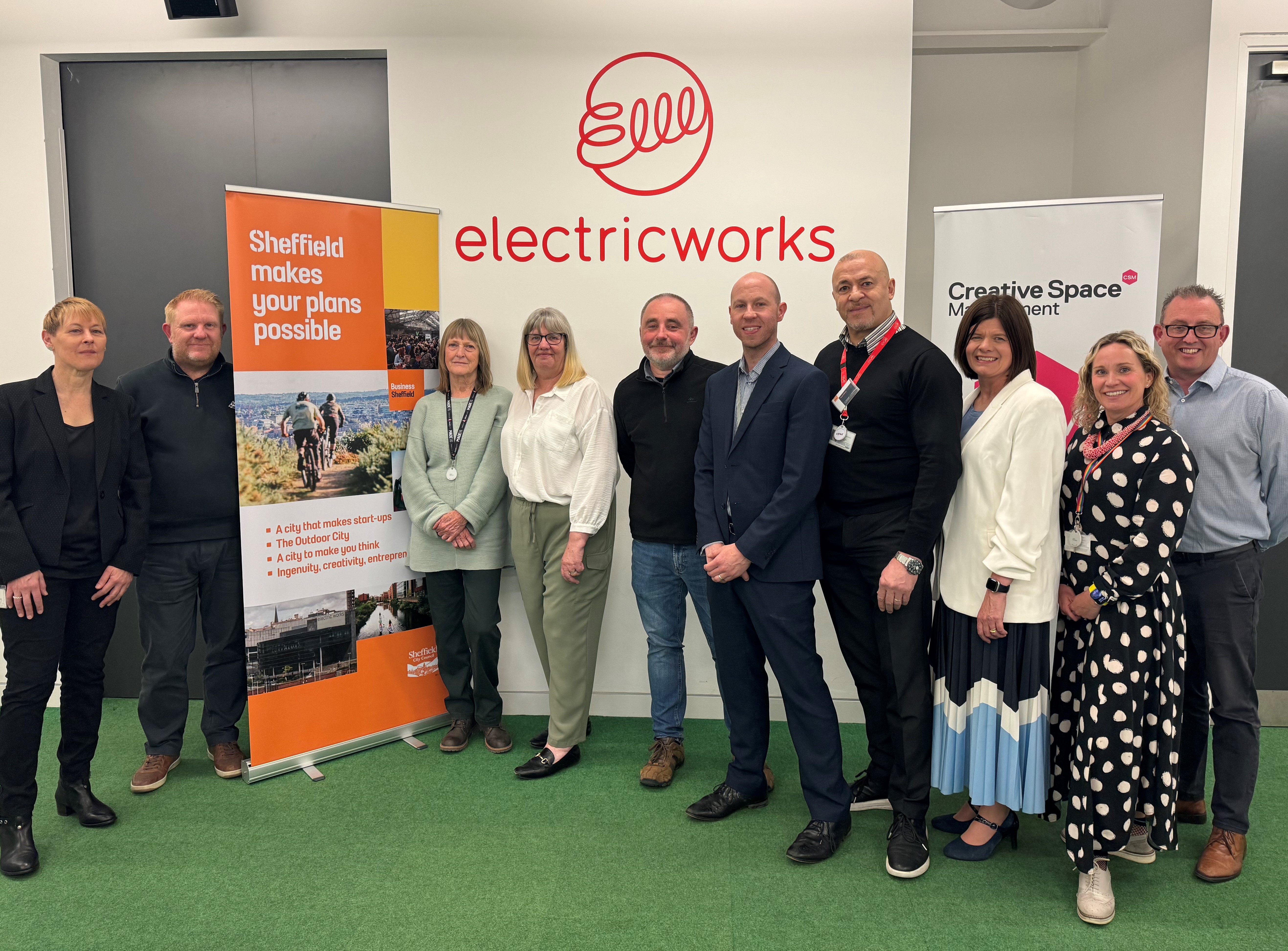 The Business Sheffield team stand smiling in front of the Business Sheffield banner at the Electric Works.