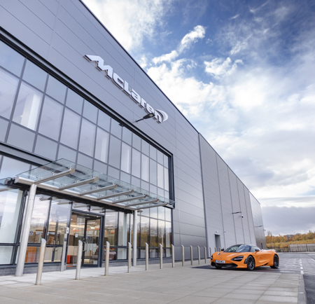 An orange McLaren car parked outside the glass McLaren building at The Advanced Manufacturing Innovation District.