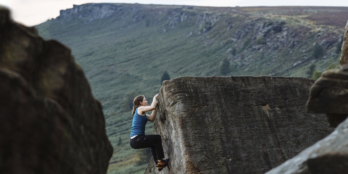 A woman climbing a rocky outcrop has nearly reached the top.