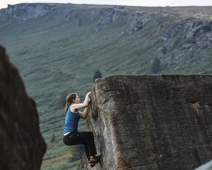 A woman climbing a rocky outcrop has nearly reached the top.