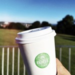 Dukes in the Park branded paper cup with the park in the background 