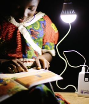 A child reads a story book, lit by a single bulb.