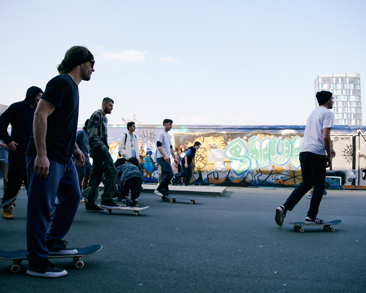 A dozen or so people are skateboarding in a small urban skate park.