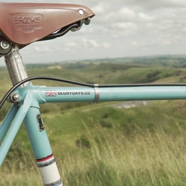 Close up of leather bike seat and bike frame, with countryside in the distance.