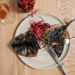 A plate with grilled fish set on a wooden table.
