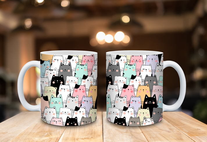 Two ceramic mugs placed on a wooden surface, each featuring a playful pattern of cartoon-style cats in pastel colors including pink, mint green, yellow, gray, and black. The background shows a softly blurred indoor setting with warm lighting.